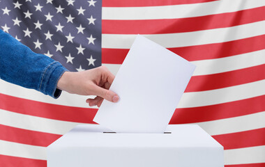 Elections, America. A human hand throws a ballot into the ballot box. American flag on the...