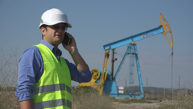 Industrial engineer talks on phone near petrol oil extraction pump
