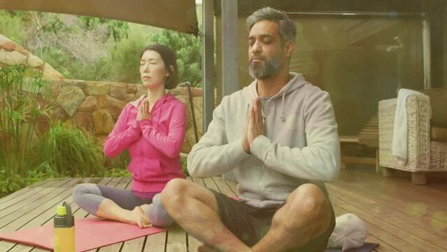 Animation of light spots over diverse couple doing yoga and meditating on terrace