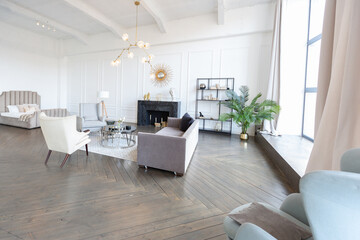 Modern luxury stylish apartment interior in pastel colors. a very bright room with huge windows filled with daylight. white walls, wooden parquet floors and a dark marble fireplace