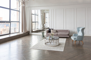 Modern luxury stylish apartment interior in pastel colors. a very bright room with huge windows filled with daylight. white walls, wooden parquet floors and a dark marble fireplace