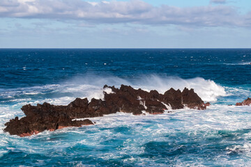Strong waves smashing against jagged volcanic rocks on pristine coastline of coastal town Porto...