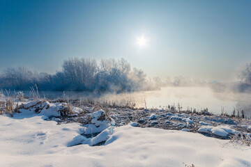 Majestic winter scenery with a foggy river with crispy rime on a trees on a snowy riverbanks. Winter wonderland.