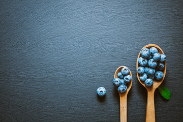 The blueberries in a wooden spoons on a black stone surface. Healthy eating concept background.