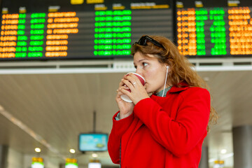 Traveler with coffee at airport flight information board