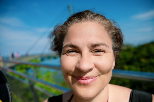 A joyful woman squints and smiles warmly under the bright sunlight at the Langkawi Sky Bridge in Malaysia