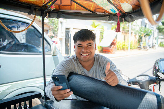 Young man in tuk tuk giving thumbs up with smartphone