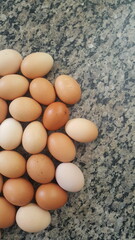 Grupo de ovos marrom, beje, e branco, sobre mesa de pedra de mármore.
