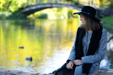 Portrait of a young girl sitting in a park on a bench near a lake.