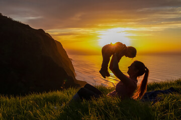 Mother lifting up child on meadow with breathtaking sunset at viewing point Miradouro do Ponta da...