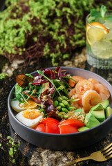 Buddha bowl salad with shrimps, arugula, spinach, avocado, tomatoes, green edamame beans, eggs on marble background. Healthy salad food, dieting, top view