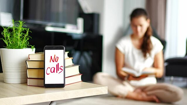 Digital detox concept photo. Smartphone with text No Calls and woman reading book in background