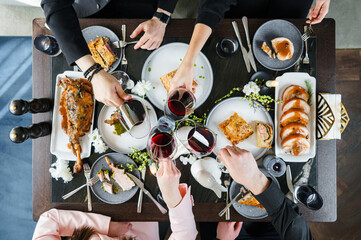 Family eating for holiday table at home. Easter holidays table with baked meat tenderloin, rib eye meat, ribs, lamb thigh, wine glasses, pies, decoration. Happy Easter concept, top view - obrazy, fototapety, plakaty