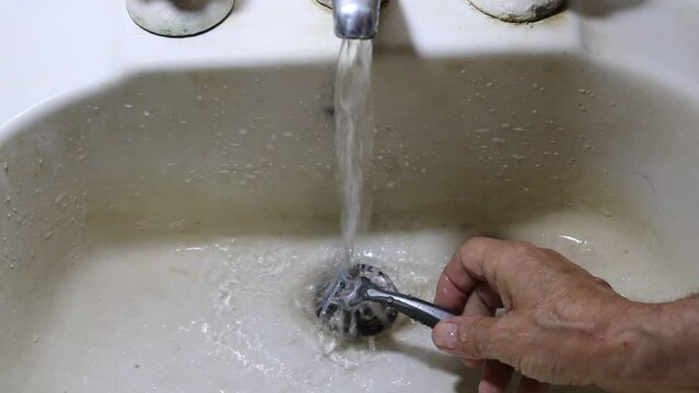 El hombre lava su navaja despu&eacute;s de afeitarse en un viejo ba&ntilde;o blanco, bajo agua corriente para limpiar la espuma de afeitar para el cuidado personal rutinario de su vida diaria