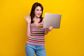 Photo of cheerful girl with stylish hairdo wear striped tank waving palm say hi on laptop video call isolated on yellow color background © deagreez