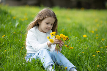 Portrait of a cute smiling little girl on green grass with dandelions