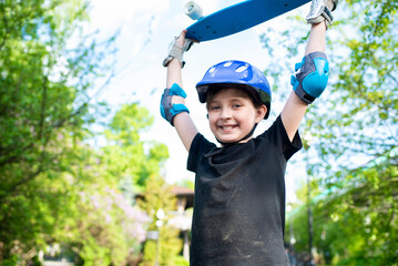 smiling 10 year old boy in a protective helmet, holding a blue skateboard in his hand, in the park...