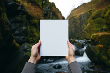 A person standing in front of a waterfall, holding a card in their hand.