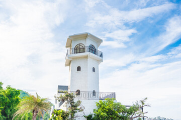 A lighthouse on a rocky shore with water in the background on a sunny day.