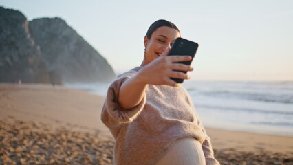 Pregnant woman video blogging on smartphone walking at sandy coast close up.