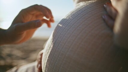 Partners hands touching pregnant tummy sitting on sunny seashore close up.