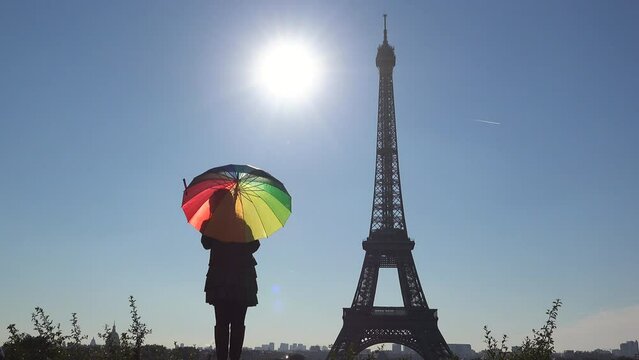 Contre-jour silhouette of lady spinning colorful umbrella in front of Eiffel Tower, Paris