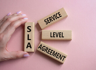 SLA - Service Level Agreement. Wooden blocks with word SLA. Businessman hand. Beautiful pink...