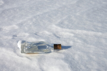 A bottle of strong alcohol on the ice of a snow-covered reservoir left by a fisherman. Copy space.