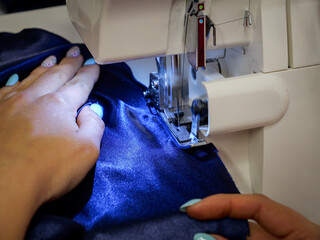 Female hand sewing on overlock machine, manufacture of clothes. Close up of sewing process in the factory.