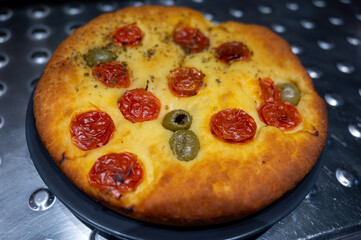 Tasty italian vegetarian food, fresh baked flat foccachia bread with cherry tomatoes, olives and herbs close up