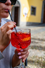 Drinking of Spritz Campari red bitter long drink cocktail maid with liqueur, prosecco sparkling wine, ice cubes and piece orange, Milan, Italy