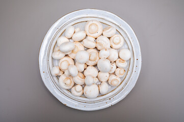 White champignon mushrooms fresh uncooked on white ceramic plate copy space
