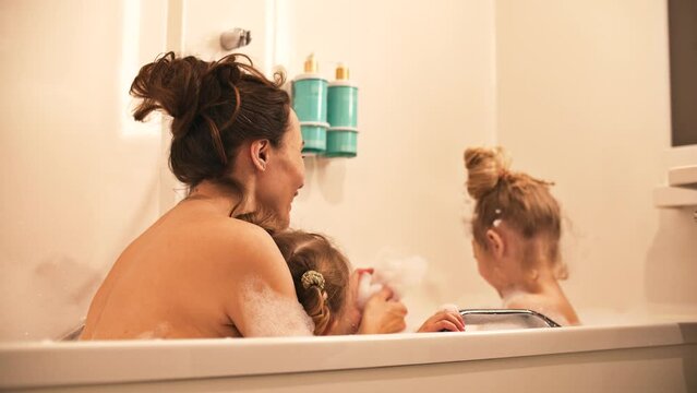 Mom and her little kids play with foam in the bathtub