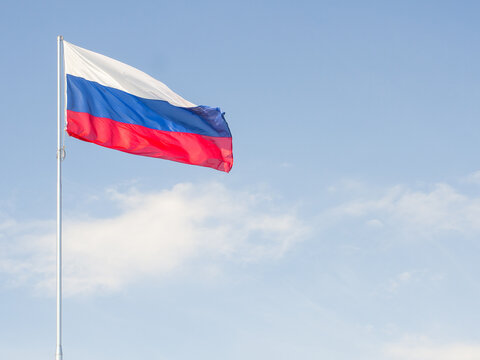 Flag of Russia waving in the wind against a blue sky with clouds