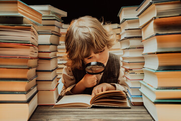 Little researcher boy reads book with magnifying glass in library. Cute clever preschooler playing,...