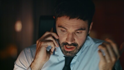 Closeup furious businessman calling sitting office late evening. Manager yelling