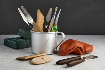 Many tools for sculpting and modeling and pieces of red clay and green plasticine on a concrete...