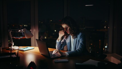 Sleepy businesswoman working night sitting at office desk. Lady looking laptop.