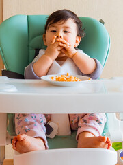 Bebe en su silla de comer usando sus manos para comer su fruta