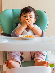 Bebe en su silla de comer usando sus manos para comer su fruta