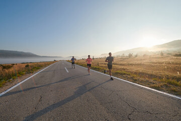 Fototapeta premium A group of friends, athletes, and joggers embrace the early morning hours as they run through the misty dawn, energized by the rising sun and surrounded by the tranquil beauty of nature