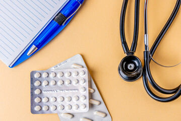 The black and steel phonendoscope, stethoscope, pills and pencil with notes on a yellow background.