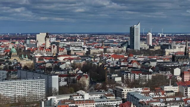 Slow flight away. Telephoto shot of the city center of Leipzig. The new town hall and other landmarks are united in the image. The old town, new buildings, wind turbines and an airplane in the sky.