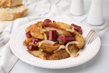 Delicious baked potato with thin dry smoked sausages and onion served on white table, closeup