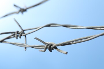 Metal barbed wire on light blue background, closeup