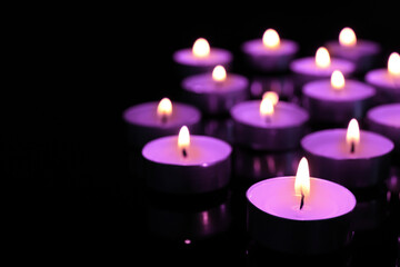 Obraz na płótnie Canvas Beautiful burning violet candles on black background. Funeral attributes