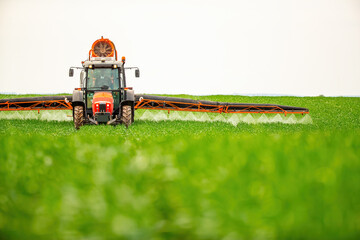 Tractor with sprayer arms extended applies treatment to crops on a vast, green farmland
