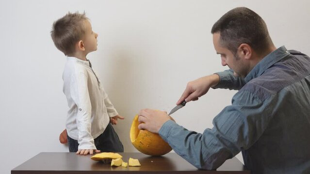 Father and son carving a Halloween jack-o'-lantern in a yellow pumpkin