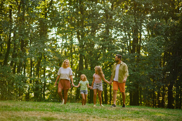 A happy family of four holding hands and taking a walk in forest.