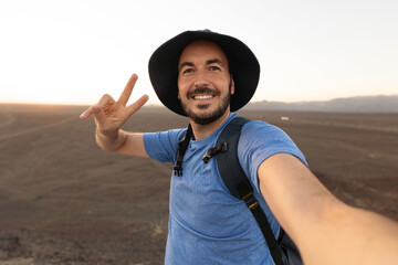 A happy man in a sun hat is smiling while taking a selfie in the desert landscape. Joyful...